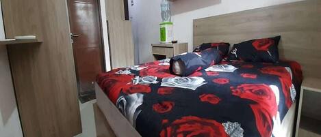 A bedroom with a bed, a wooden headboard, a nightstand, a water dispenser, and a wardrobe.