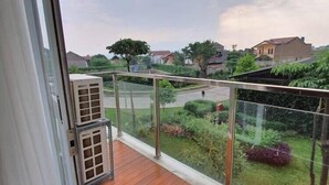 A balcony with a wooden floor, glass railing, and a view of a residential area with houses and greenery. - Gateway Pasteur Apartment Bandung (Cimahi)