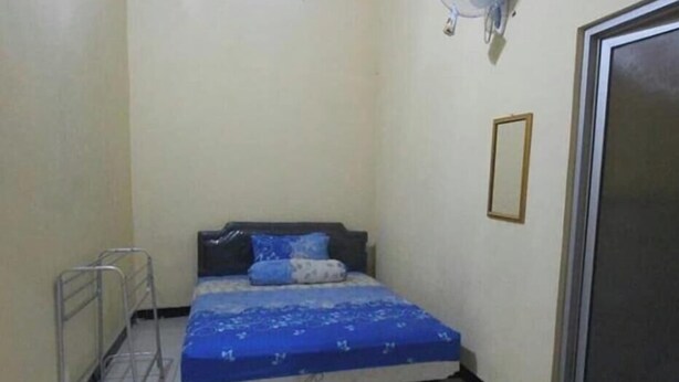 A small, narrow room with a bed, a window, a wall-mounted fan, and a door. - Homestay Sekar (Borobudur)