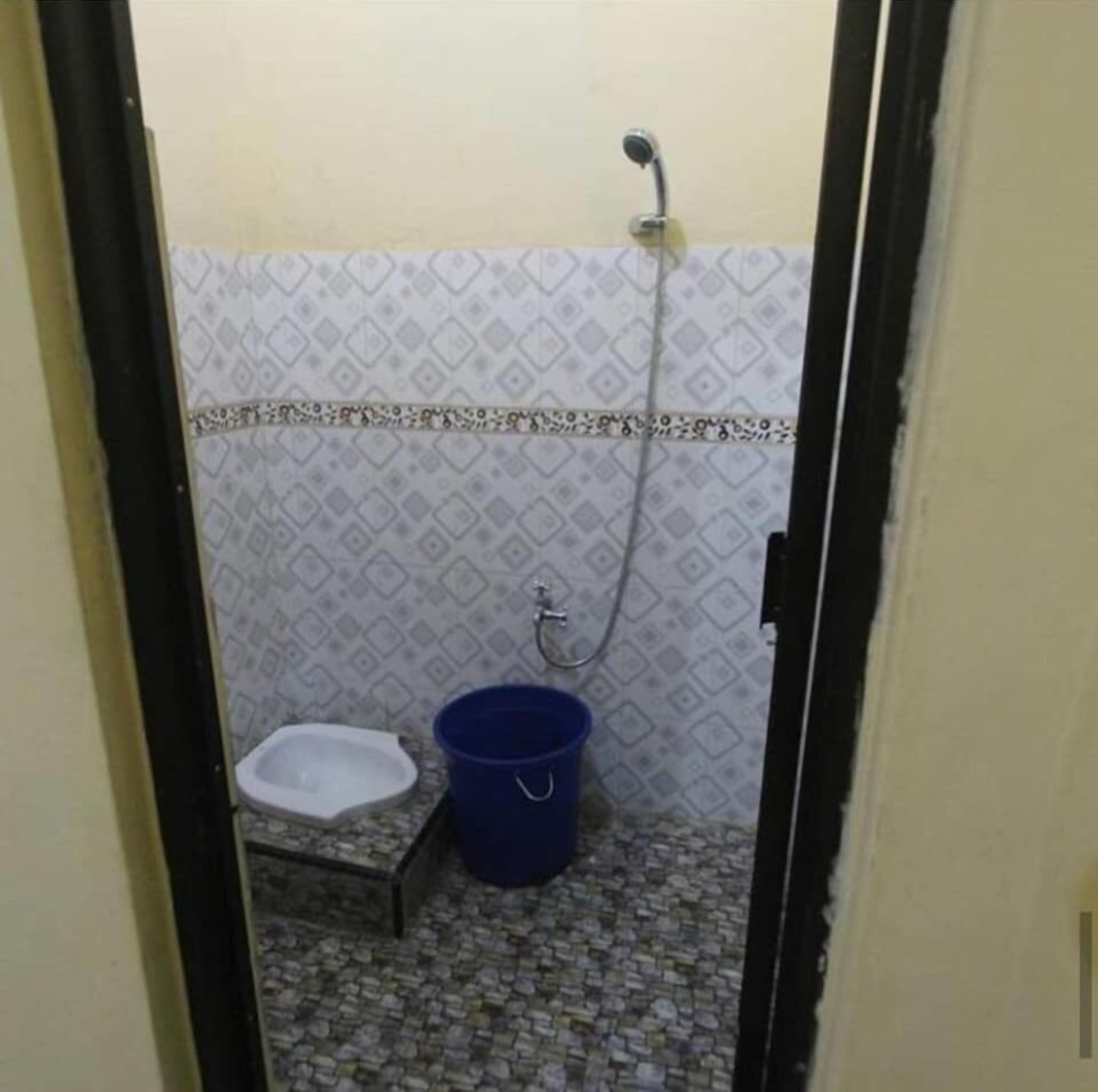 A small bathroom with a toilet, a blue bucket, and a shower.