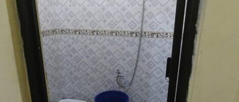 A small bathroom with a toilet, a blue bucket, and a shower.