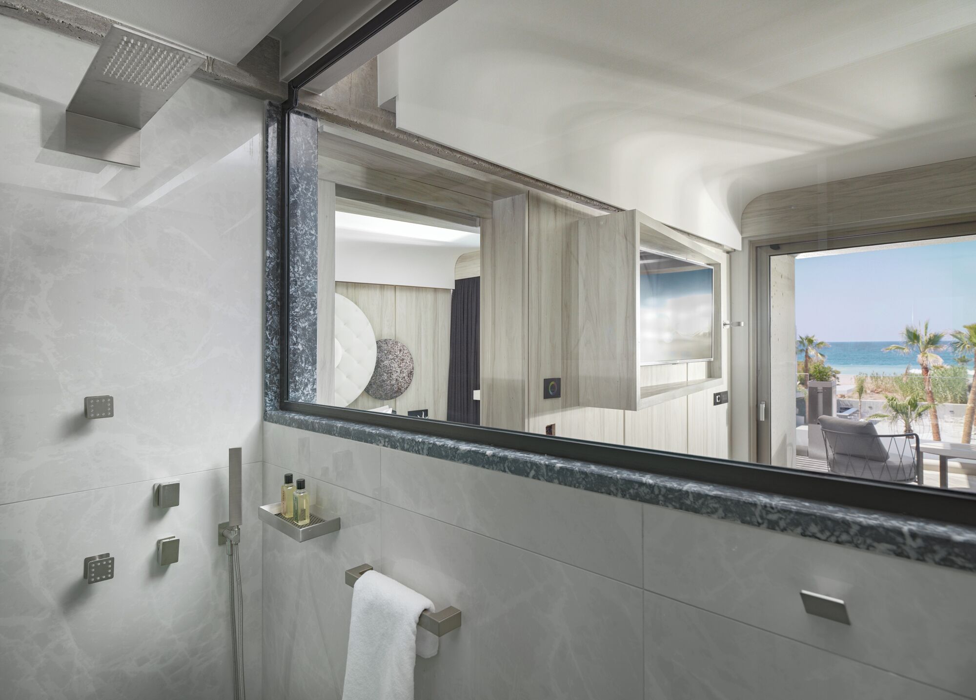 A modern bathroom with a large mirror, a shower, and a view of the beach.