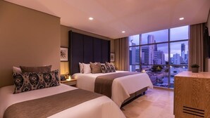 A hotel room with two beds, a large window with a city view, and a wooden side table. - Hotel OZ Luxury (Cartagena (CO))