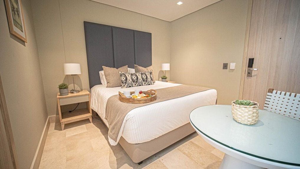 A hotel room with a bed, bedside tables, a glass table, and a door.