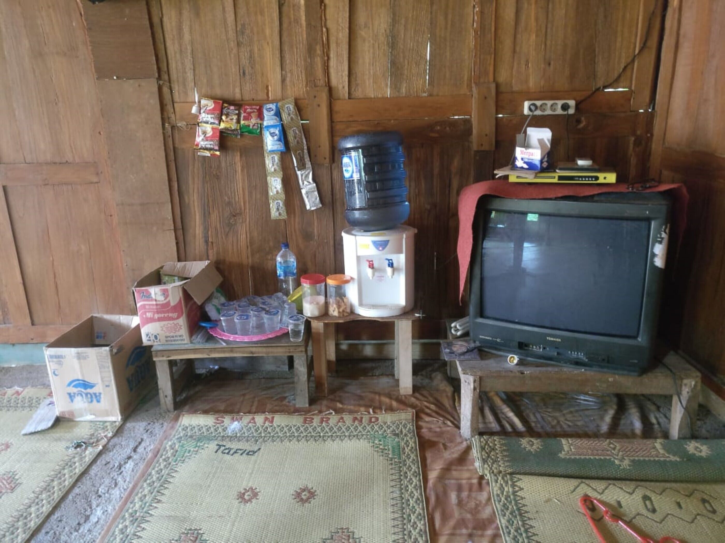 A room with a wooden wall, a television, a water dispenser, and various items on a small table.