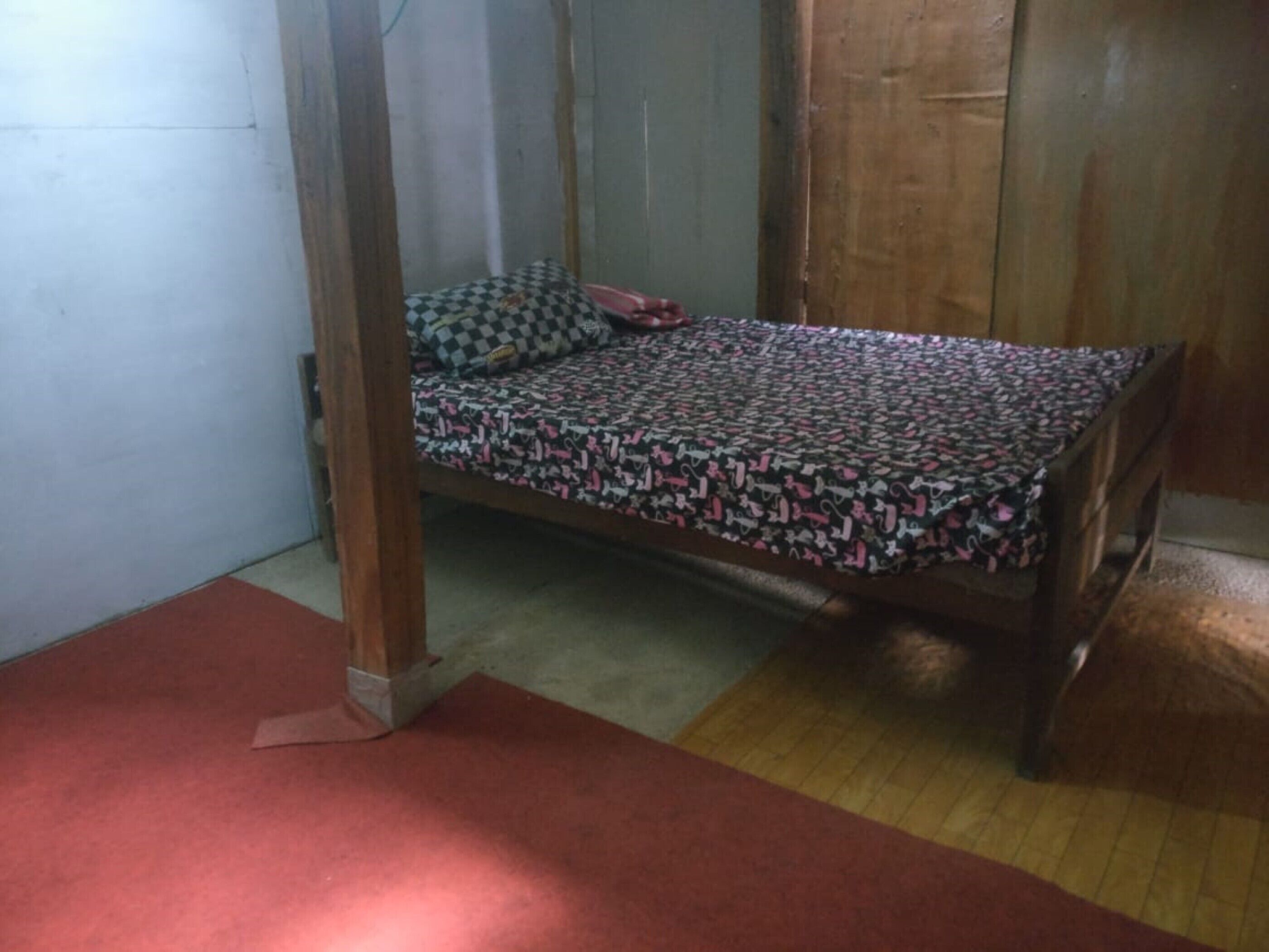 Un lit simple avec une couvre-lit à motifs, dans une pièce aux murs en bois et au tapis rouge.
