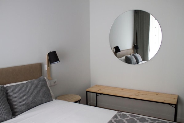 A bedroom with a bed, a bedside table, a mirror, and a bench.