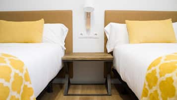 Una habitación de hotel con dos camas, una mesita de noche, una lámpara y un enchufe en la pared.