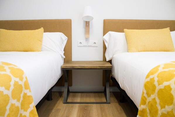 Una habitación de hotel con dos camas, una mesita de noche, una lámpara y un enchufe en la pared.