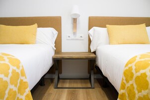 A hotel room with two beds, a nightstand, a lamp, and a power outlet on the wall.