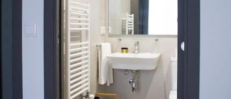 A hotel room with a bed, a bathroom with a sink and mirror, and a window with curtains.