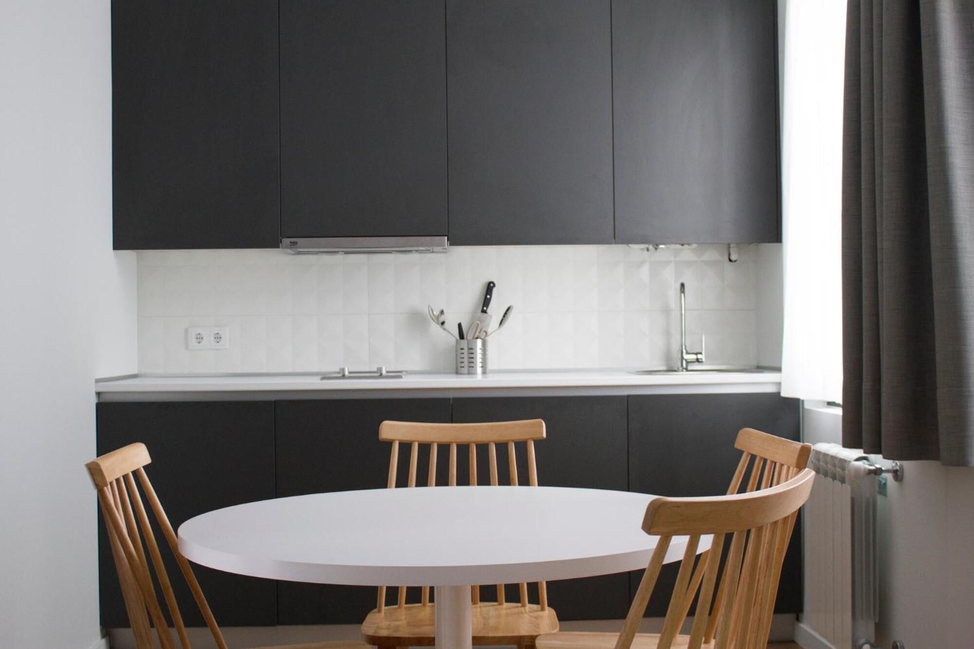 Una cocina moderna con armarios oscuros, una encimera blanca y una mesa redonda con sillas de madera.