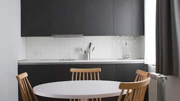 Una cocina moderna con armarios oscuros, una encimera blanca y una mesa redonda con sillas de madera.