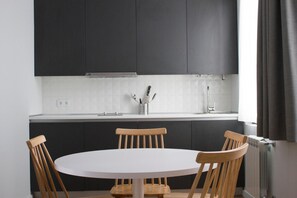 Una cocina moderna con armarios oscuros, una encimera blanca y una mesa redonda con sillas de madera.