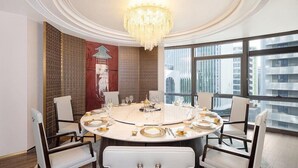Une salle à manger avec une table ronde dressée pour six personnes, de grandes fenêtres et un lustre.