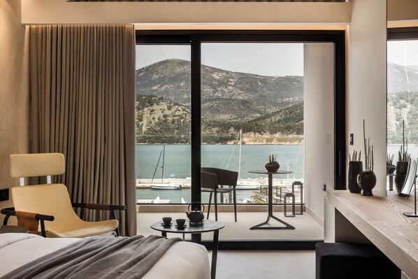 Una habitación de hotel con cama, una silla, una mesita con tetera y vistas a un cuerpo de agua y montañas.
