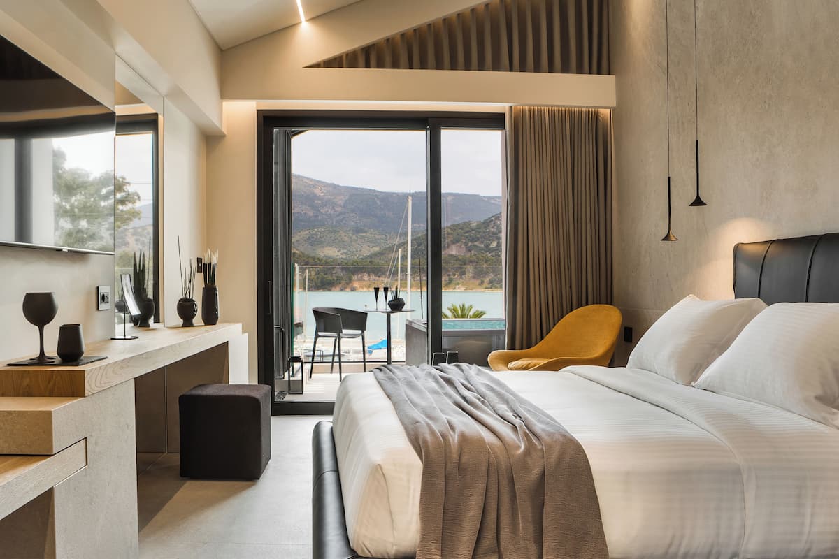 A modern hotel room with a large bed, a desk, and a balcony with a view of the hills.