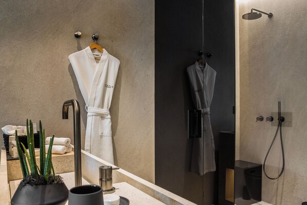 A modern bathroom with a large mirror, a sink, a shower with a handheld showerhead, and two robes hanging on hooks. - Canale Hotel & Suites (Kefalonia)