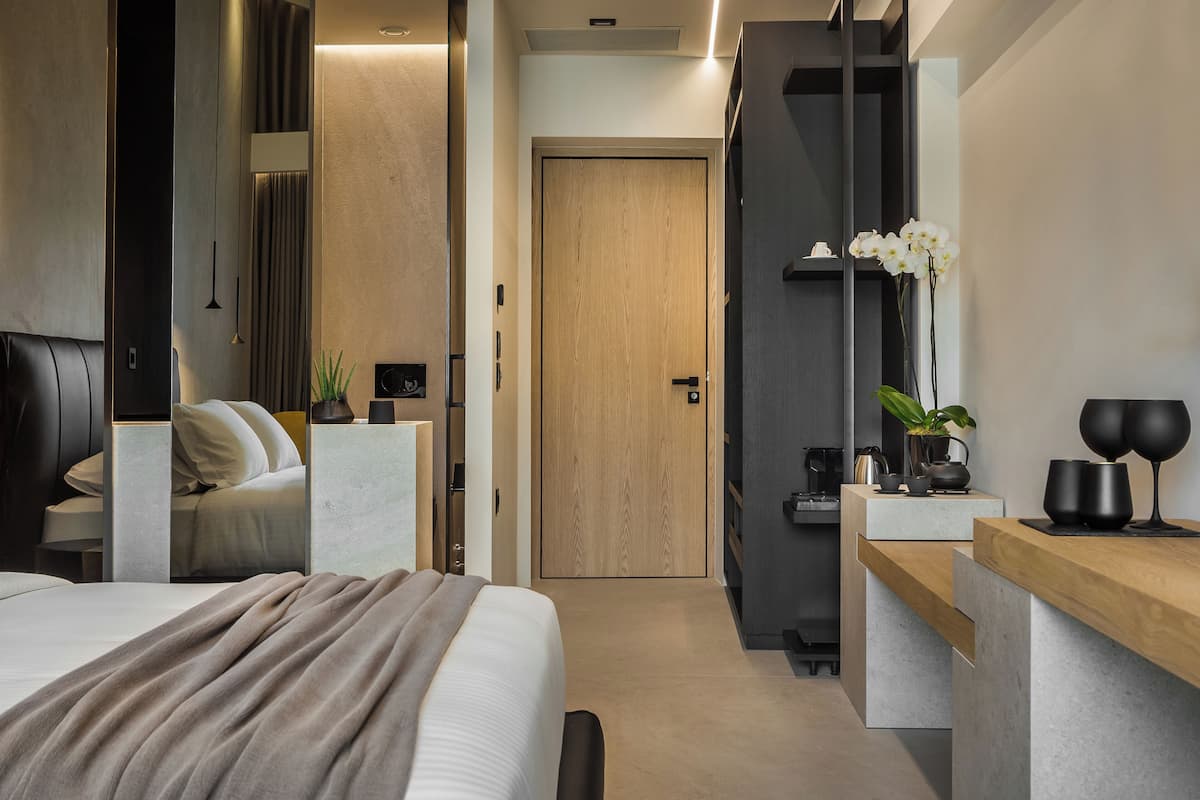 A modern hotel room with a bed, bedside table, and a small desk with a chair.