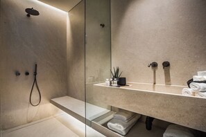 A modern bathroom with a glass shower enclosure, a vanity with a mirror, and neatly folded towels. - Canale Hotel & Suites (Kefalonia)
