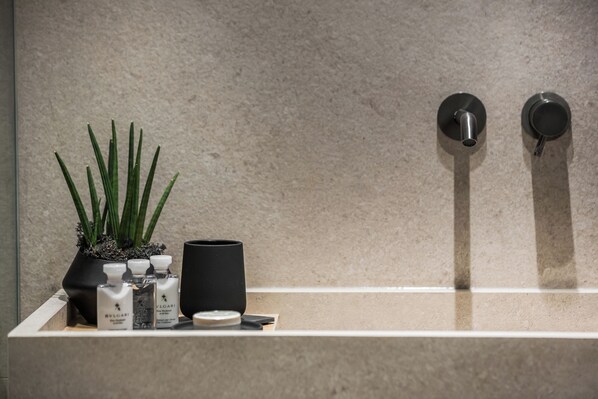 A bathroom with a sink, a potted plant, and toiletries. - Canale Hotel & Suites (Kefalonia)