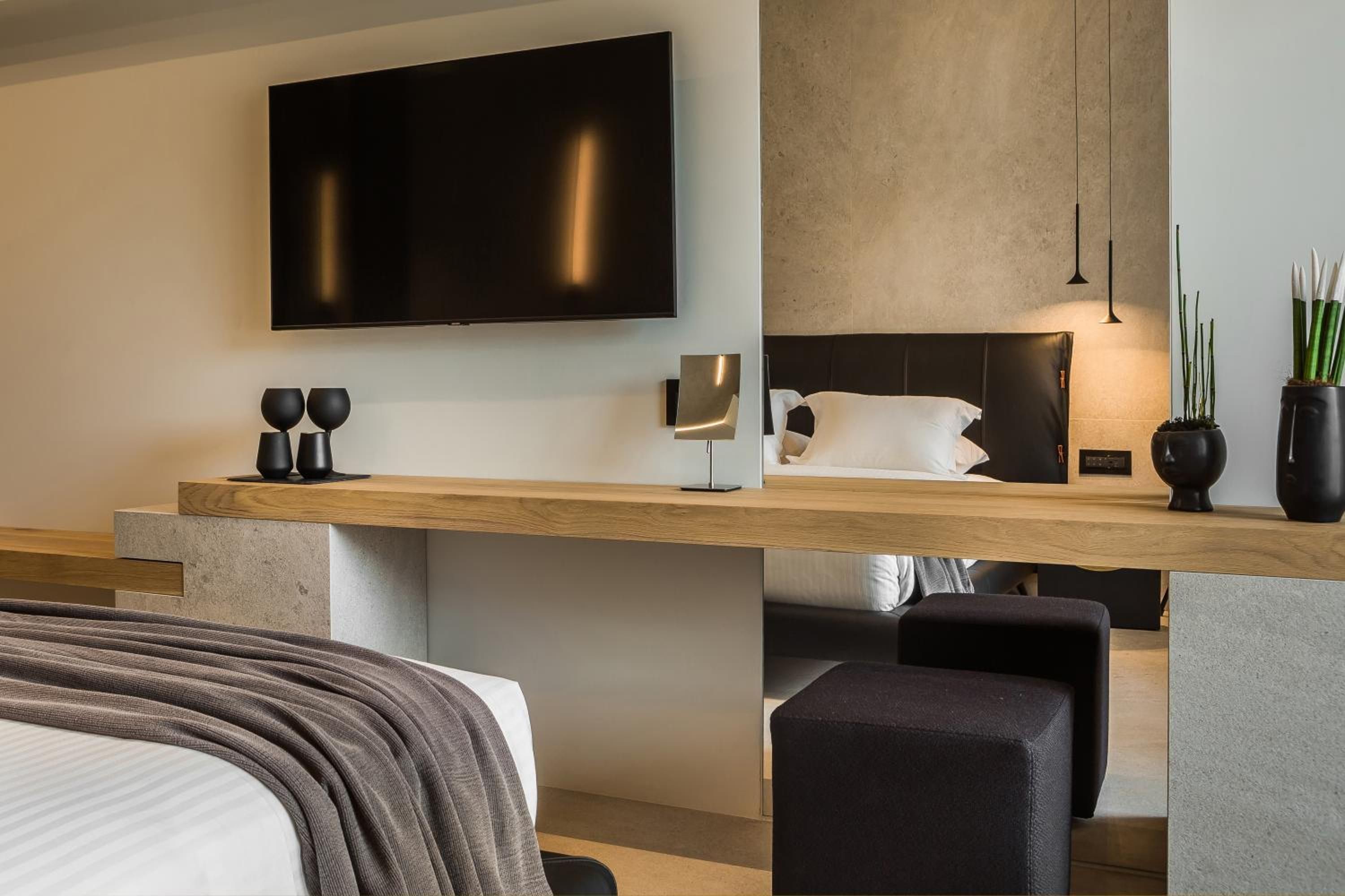 Una habitación de hotel moderna con un televisor de pantalla plana grande, un escritorio de madera, una cama con cabecera y un pequeño rincón de descanso.