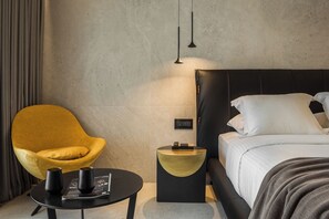 A modern hotel room with a bed, a round table with two black cups, a yellow chair, and a small side table with a lamp. - Canale Hotel & Suites (Kefalonia)
