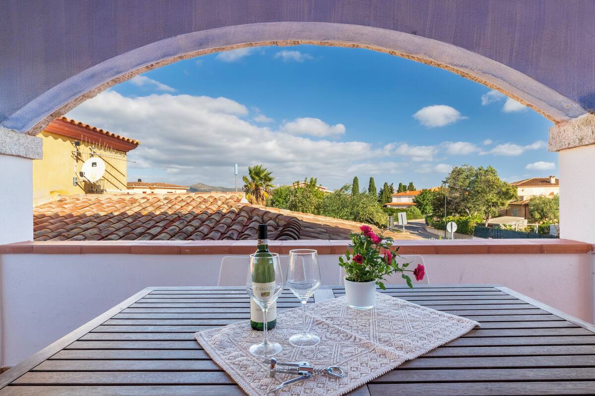 A balcony with a table set for two, a bottle of wine, and a potted plant.