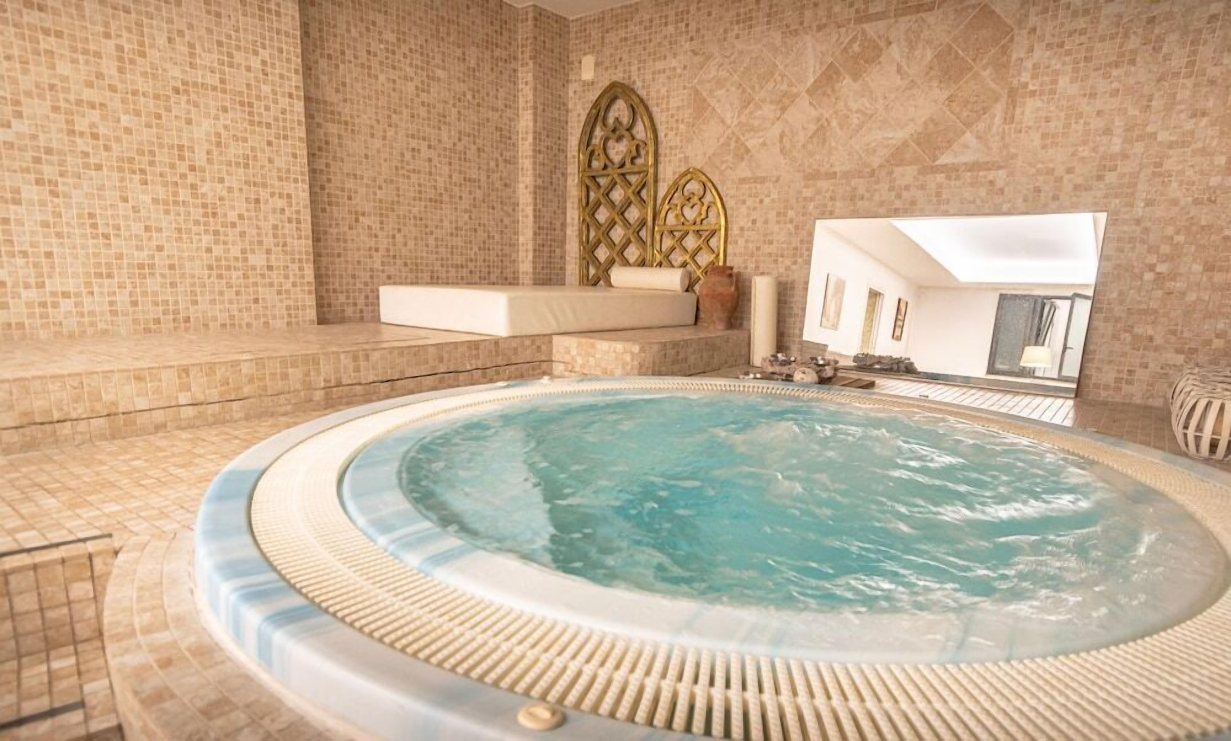 Et spa-område med jacuzzi, opholdsområde med polstret bænk og en dekorativ væg med geometrisk mønster.