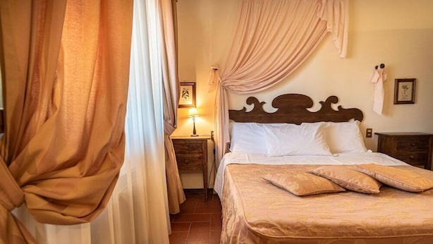 A bedroom with a bed, curtains, a nightstand, and a wall-mounted lamp. - San Crispino Resort and Spa (Assisi)