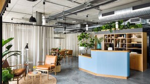 A modern reception area with a blue counter, wooden shelves, and potted plants. - Turing Locke, Eddington (Cambridge)