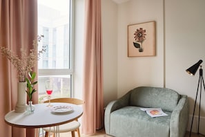 A room with a round table, a green armchair, a framed floral artwork, and a vase with flowers. - Turing Locke, Eddington (Cambridge)