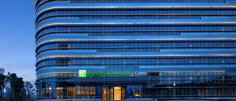 A modern hotel with a curved facade, large glass windows, and a prominent entrance with a green sign.