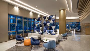 A modern lobby with seating areas, large windows, and a decorative wall.