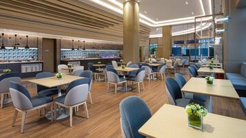 Een modern restaurant met diverse zitmogelijkheden, waaronder tafels, zitjes en een bar, met een toonbank waar eten gepresenteerd wordt.