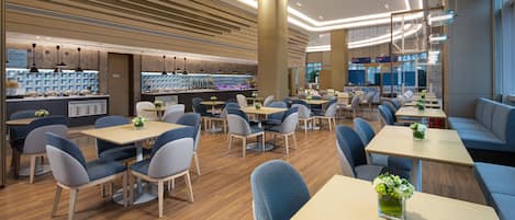 Un restaurante moderno con diversas opciones de asientos, incluyendo mesas, cabinas, una zona de bar y un mostrador con exhibición de alimentos.