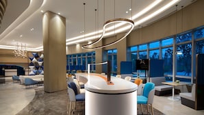 En moderne hotellobby med en central reception, siddeområder og store vinduer.