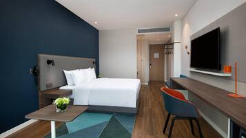 Een moderne hotelkamer met een bed, een bureau, een stoel, een televisie en een klein tafeltje met een bloevas.
