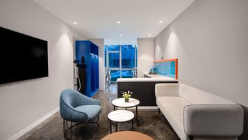 Habitación de hotel moderna con sofá, dos sillones, una mesita redonda, televisor de pantalla plana y vistas al exterior.