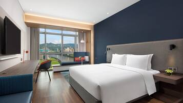 A modern hotel room with a large bed, a desk, a TV, and a view of the city.