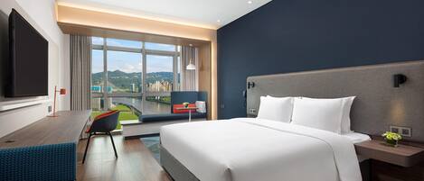 Una habitación de hotel moderna con una cama grande, un escritorio, un televisor y vistas a la ciudad.