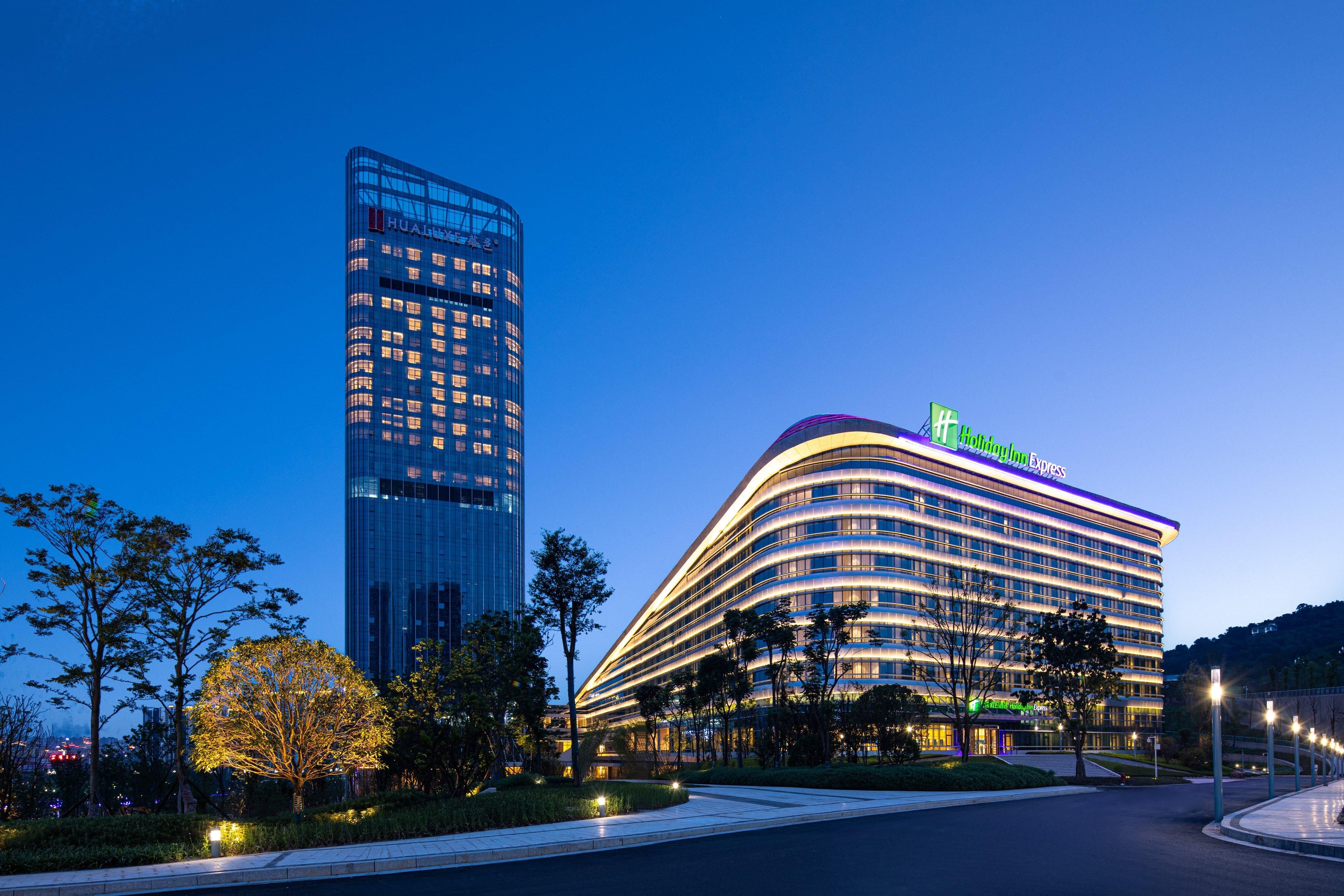 A modern hotel with a curved facade, a prominent sign, and a tall adjacent building.