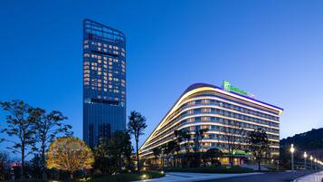A modern hotel with a curved facade, a prominent sign, and a tall adjacent building.