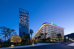 Un hotel moderno con fachada curva, un letrero llamativo y un edificio alto contiguo.