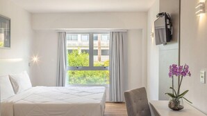 Ein Hotelzimmer mit einem Bett, einem Schreibtisch, einem Stuhl, einem an der Wand befestigten Fernseher und einem Fenster mit Vorhängen.
