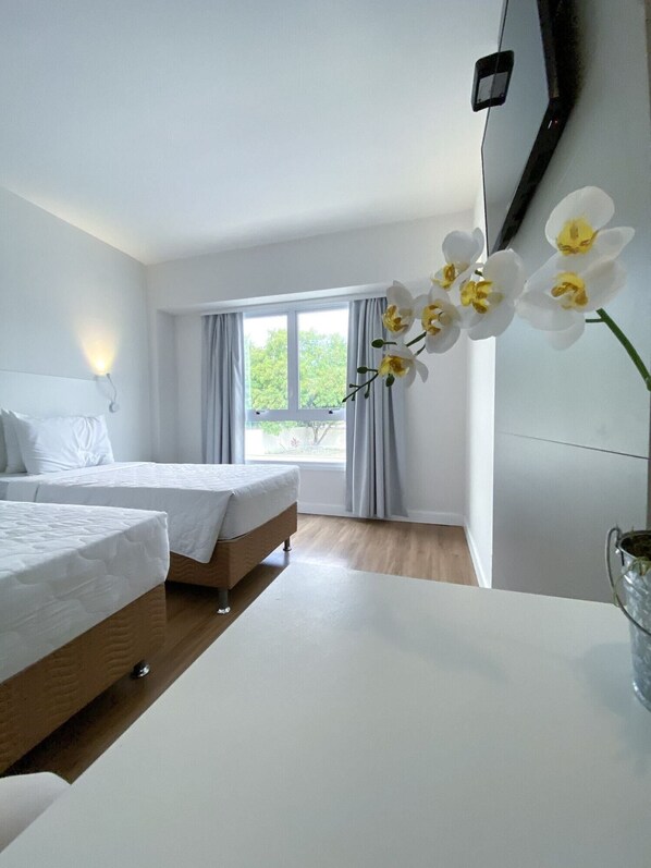 A hotel room with two beds, a window with curtains, and a vase with flowers on a table. - ATH Hotel - Américas Townhouse (Rio de Janeiro)