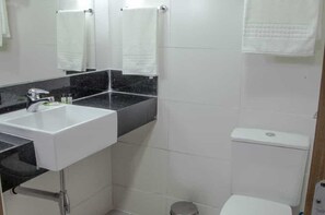 A bathroom with a white sink, black countertop, white tiles, a toilet, and a mirror. - ATH Hotel - Américas Townhouse (Rio de Janeiro)
