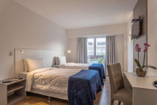 A hotel room with two beds, a desk, a chair, a TV, and a window with curtains.