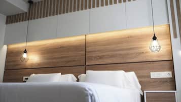 Una habitación de hotel moderna con cabecera de madera, dos lámparas colgantes y ropa de cama blanca.
