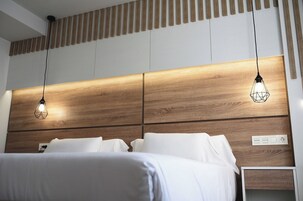 Una habitación de hotel moderna con cabecera de madera, dos lámparas colgantes y ropa de cama blanca.
